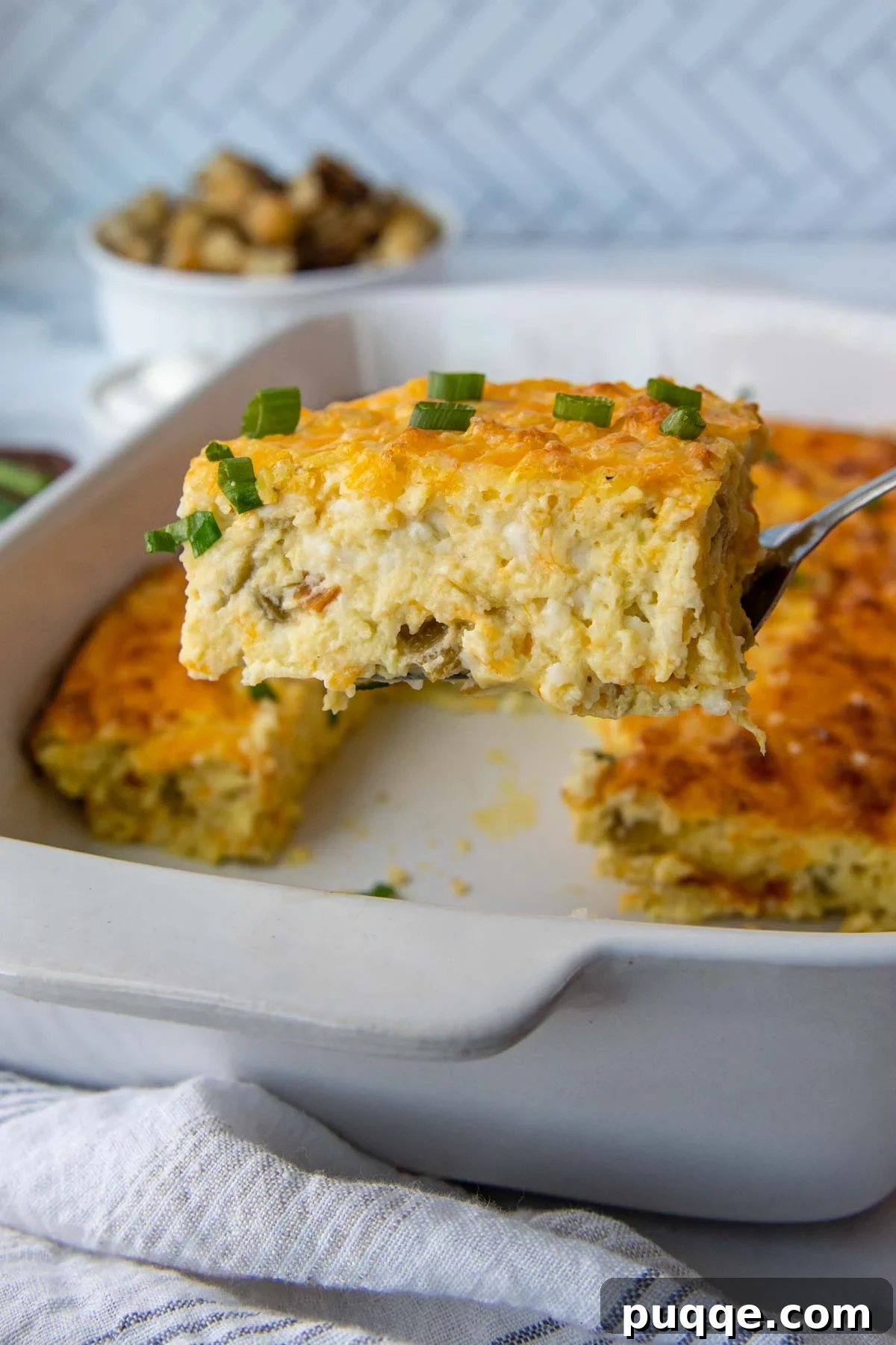 A spatula lifting out a golden-brown slice of Egg Green Chile Casserole, showcasing its fluffy texture and cheesy interior.