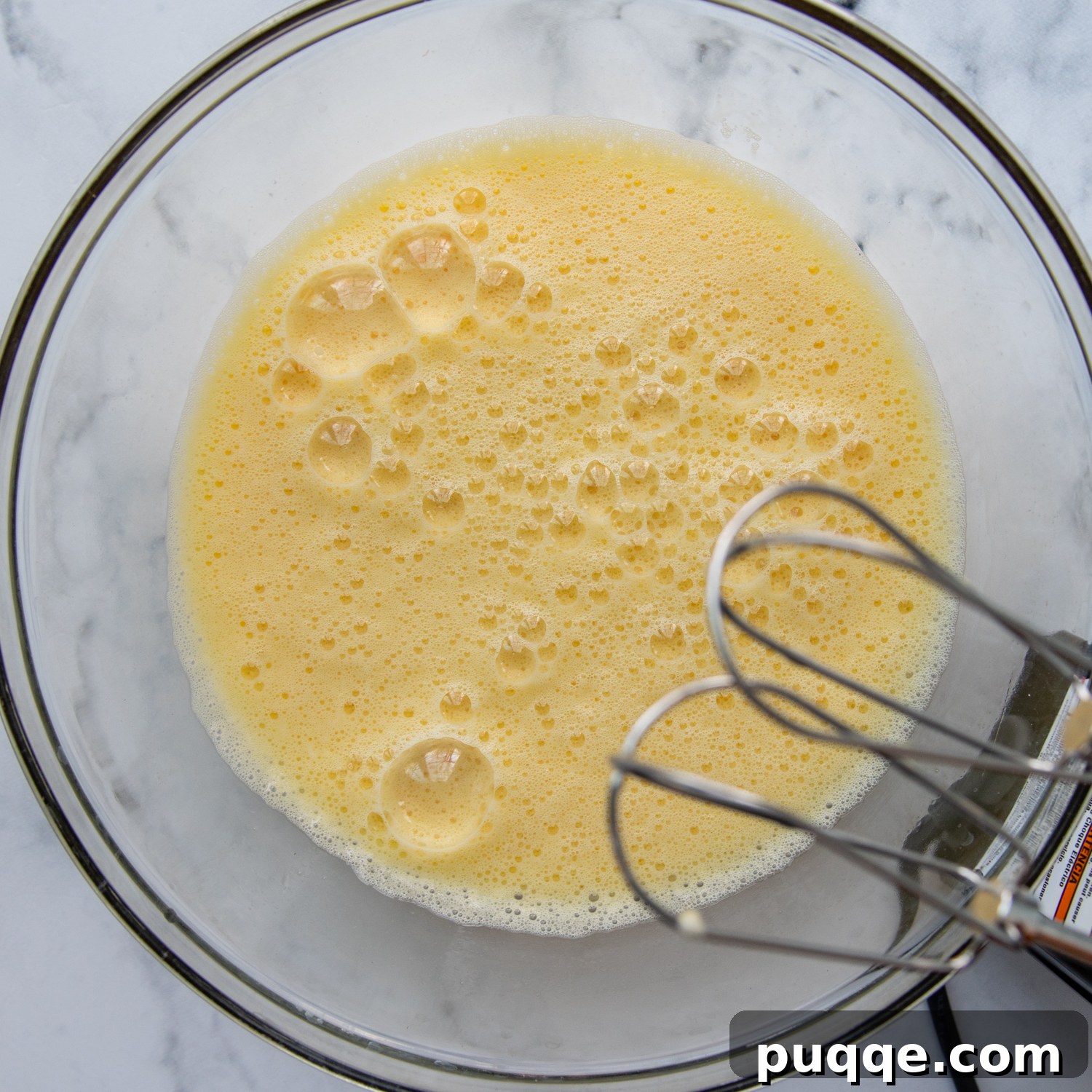 Large eggs being beaten in a spacious mixing bowl, creating a light and frothy mixture.