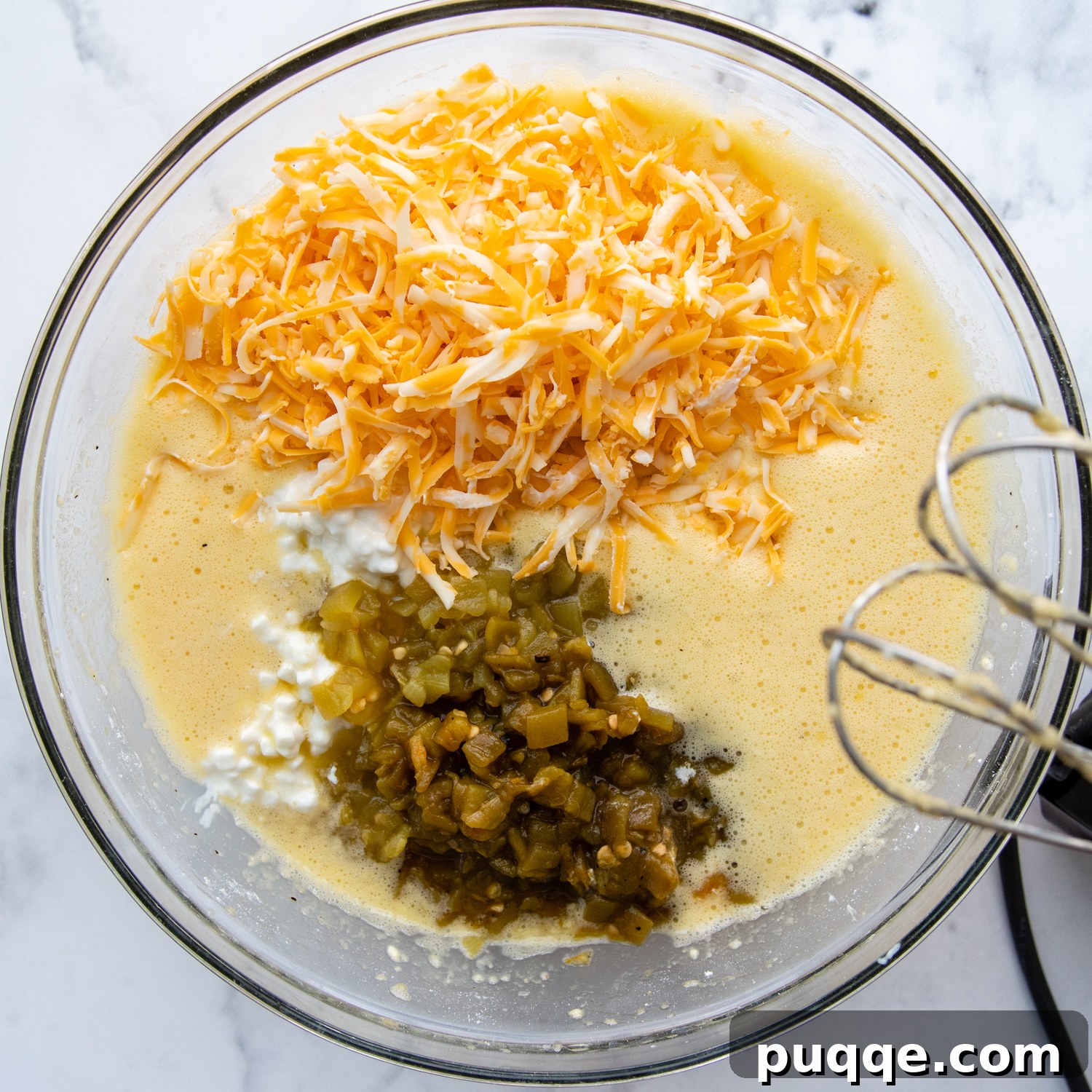 A mixing bowl filled with the egg mixture, green chiles, cheese, and cottage cheese, ready to be combined.