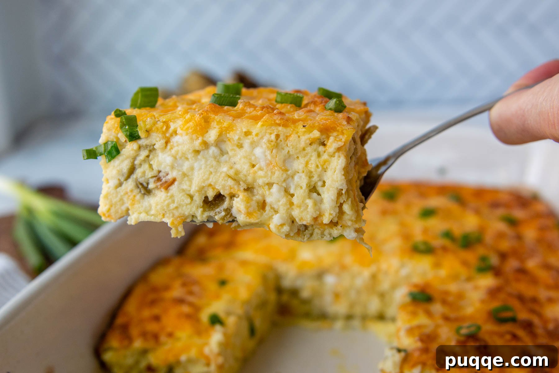 A slice of green chile egg casserole being delicately lifted from the baking dish with a spatula, revealing its golden crust and creamy interior.