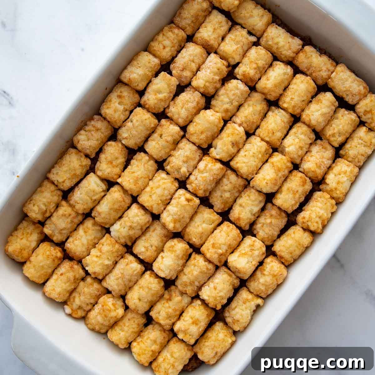 Golden Tater Tot Sloppy Joe Bake 7 Frozen tater tots neatly arranged in rows on top of the sloppy joe meat mixture in a casserole dish, ready for baking.