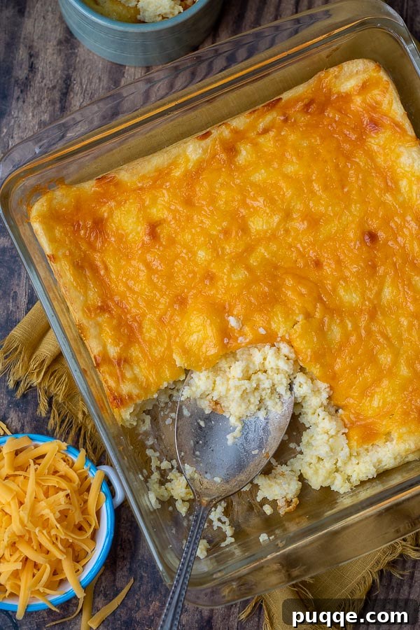 An overhead shot of a warm cheese grits casserole with shredded cheese ready to melt on top.