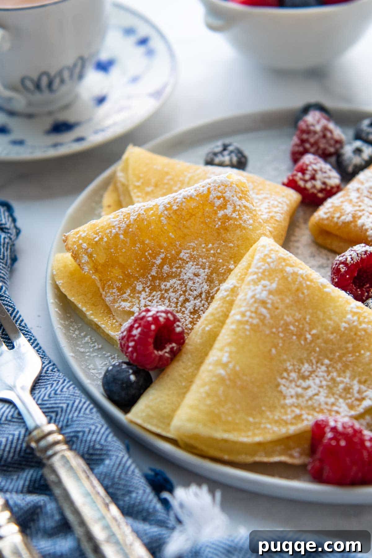 A close-up shot of perfectly folded gluten-free crepes, scattered with fresh berries.