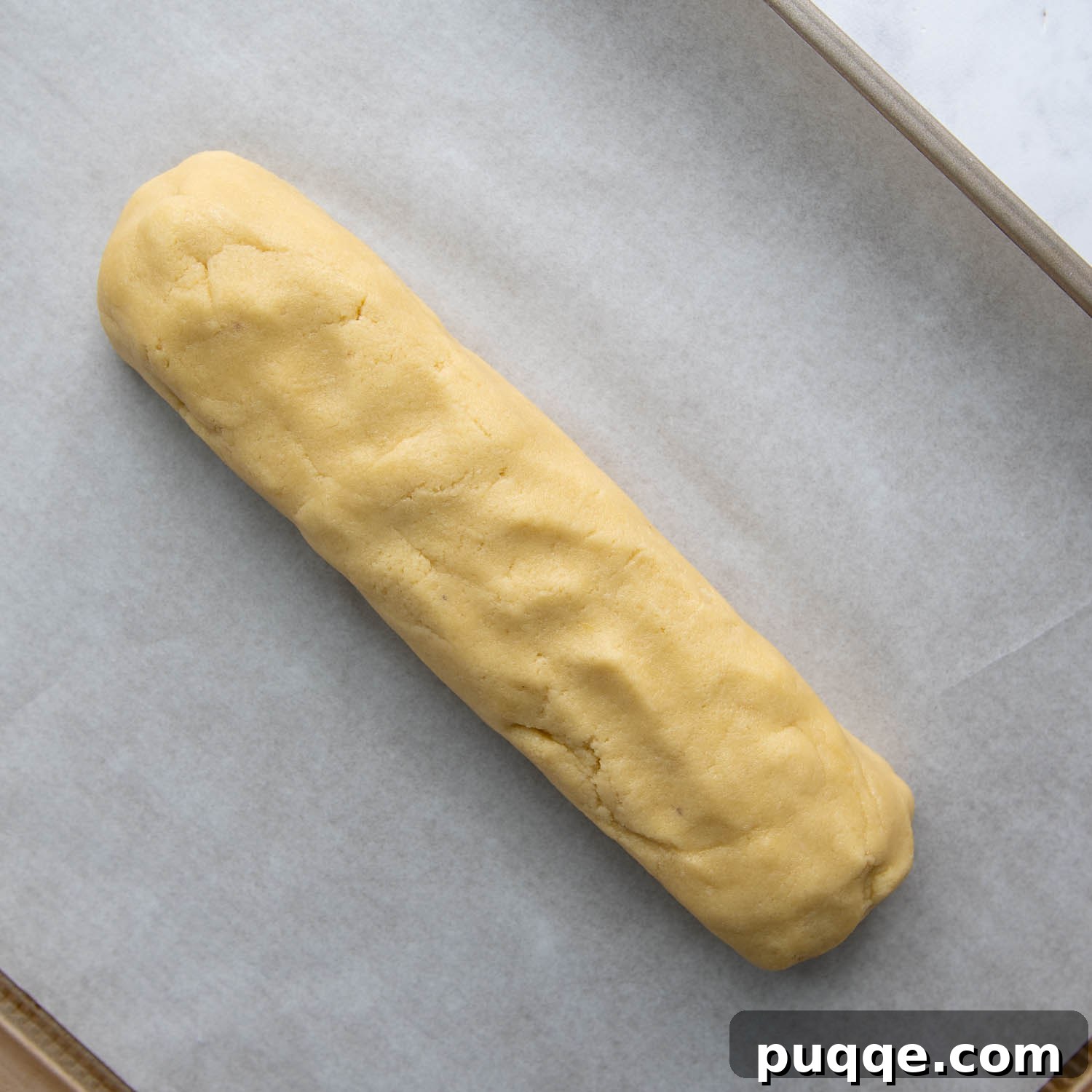 The biscotti dough expertly shaped into a long, thick log on a parchment-lined baking sheet.