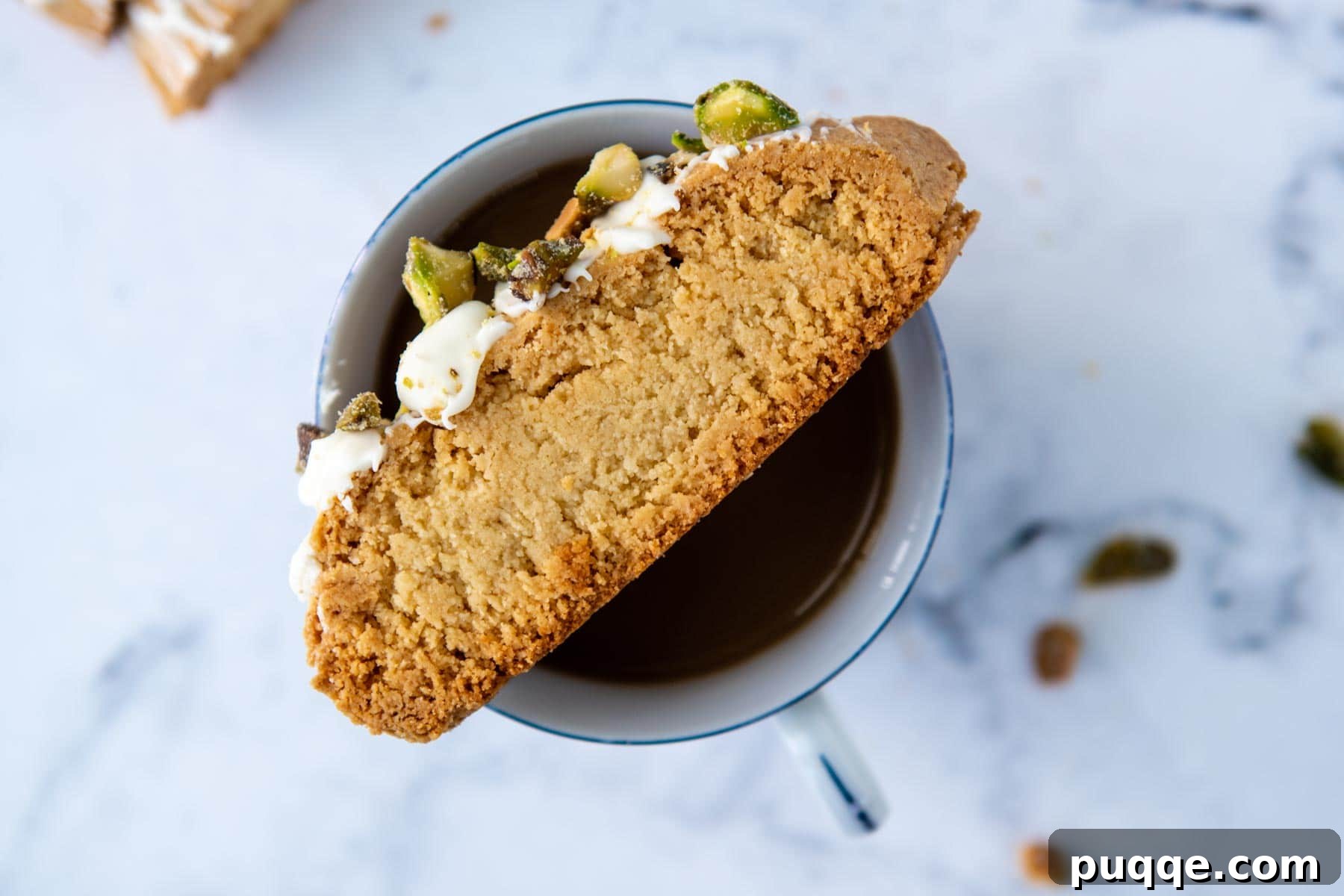 A piece of almond flour biscotti artfully balanced on the rim of a coffee cup, highlighting its inviting texture.