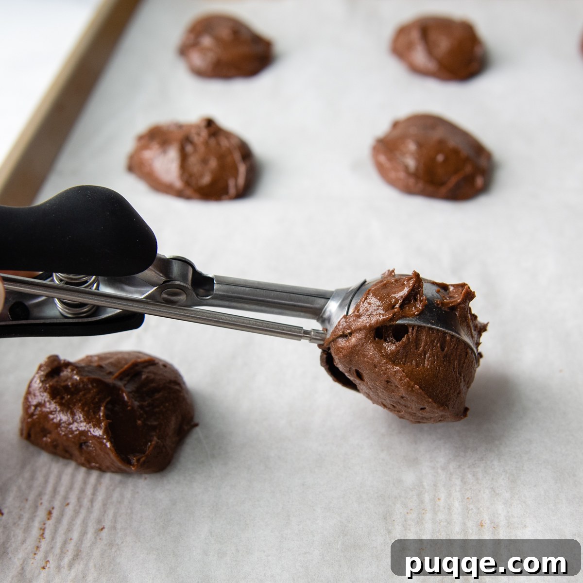Grandma's Easy Gluten-Free Whoopie Pies 4 A cookie scoop precisely portioning chocolate whoopie pie batter onto a parchment-lined baking sheet, preparing for baking.