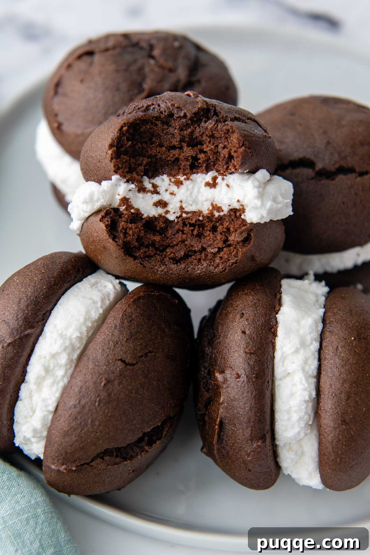 Grandma's Easy Gluten-Free Whoopie Pies 8 A beautifully arranged stack of homemade gluten-free whoopie pies on a plate, with one piece showing a bite taken out, revealing the soft chocolate cake and creamy white filling.