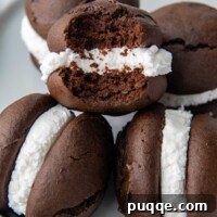 A stack of perfectly formed gluten-free whoopie pies on a plate, with one missing a bite, revealing the luscious filling.