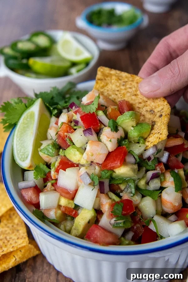 A crispy tortilla chip perfectly scooping up a vibrant and refreshing shrimp avocado salsa, hinting at delicious flavor.