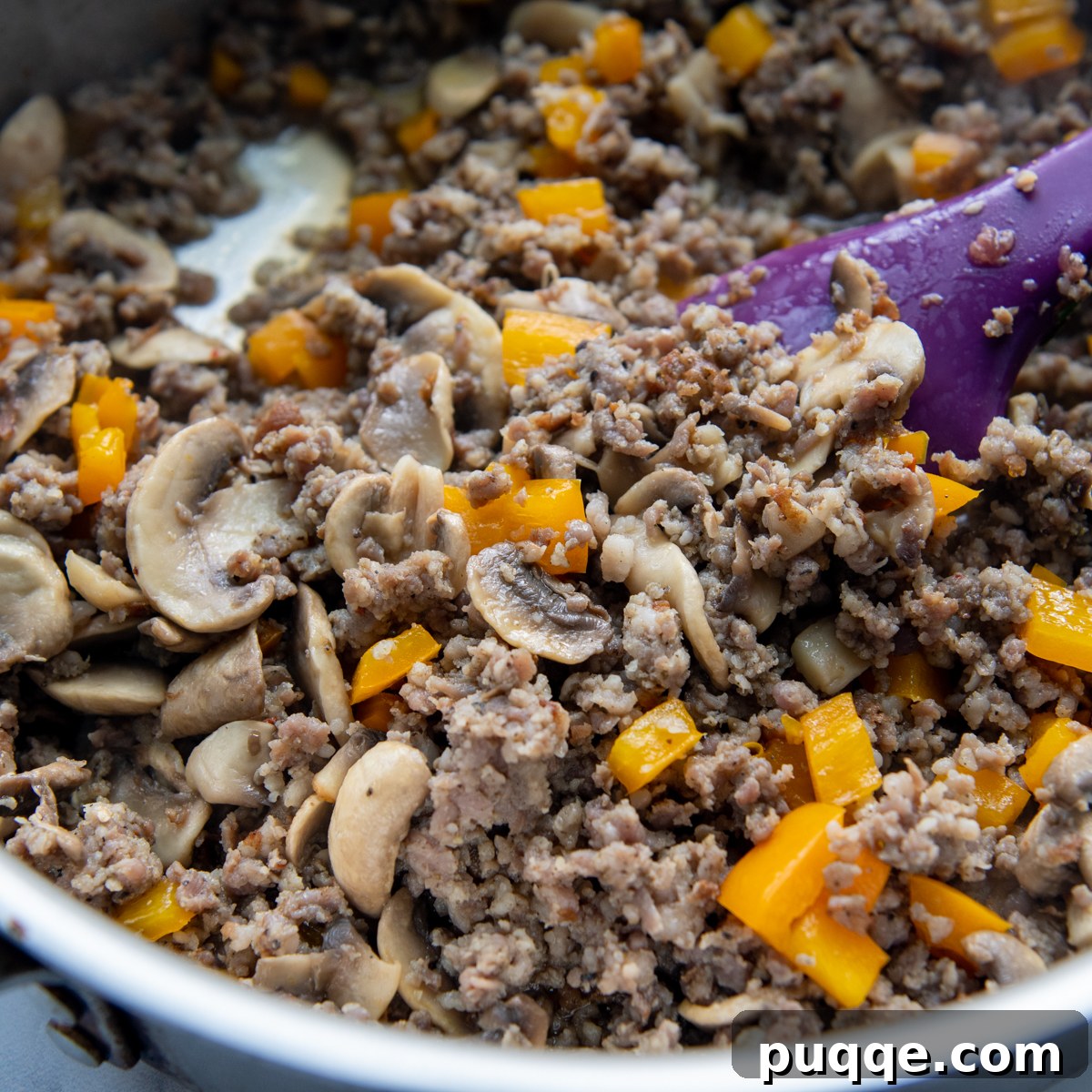 Sausage, mushrooms, and peppers cooking in a large skillet until browned and tender.