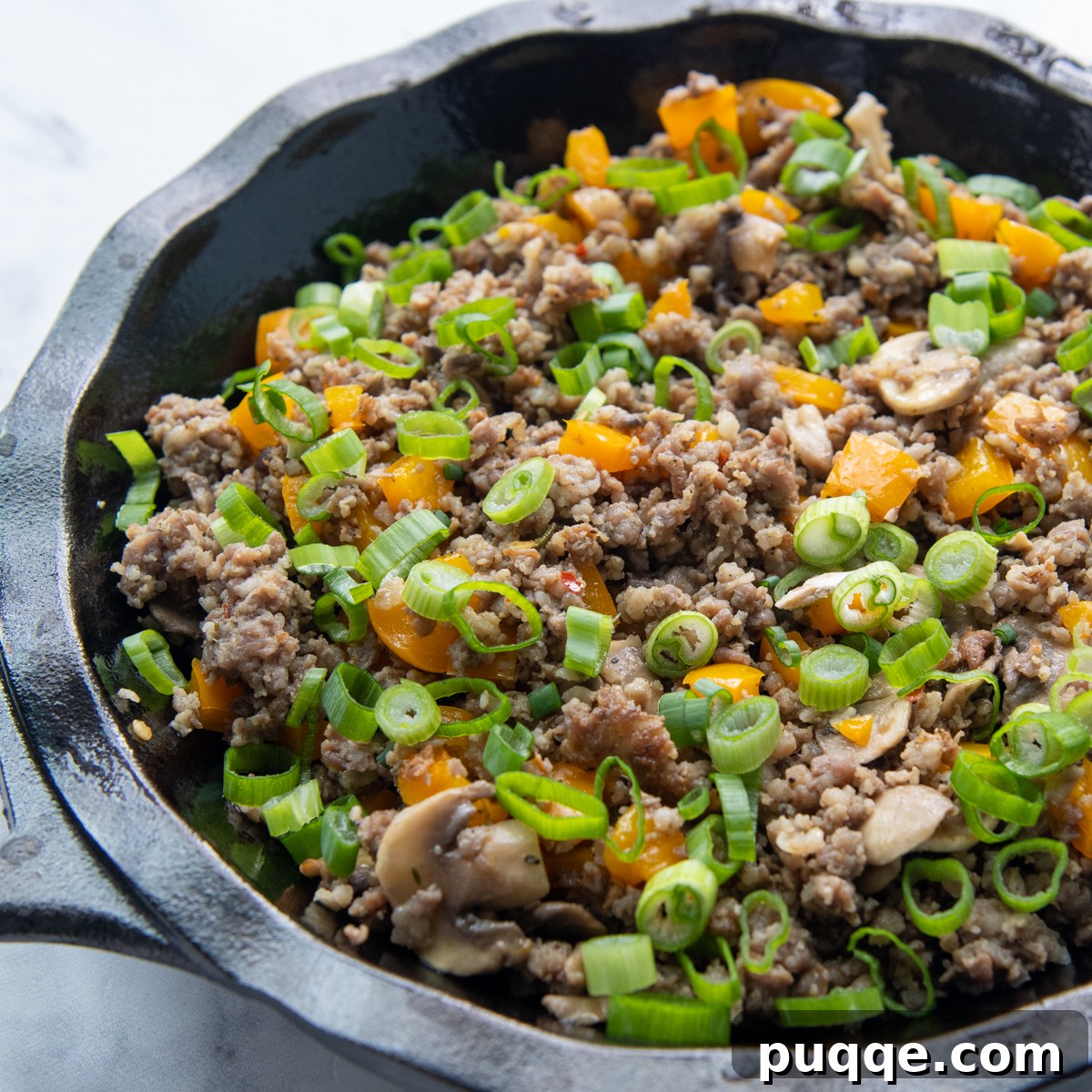 The cooked sausage and vegetable mixture, topped with green onions, layered in a pie plate.