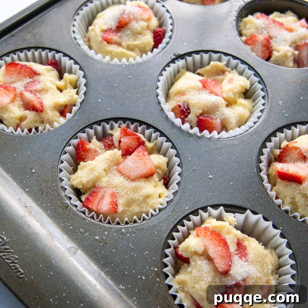 Light and Fluffy Gluten-Free Strawberry Muffins 4 Unbaked gluten-free strawberry muffins in a muffin pan, sprinkled with turbinado sugar for a crunchy topping.