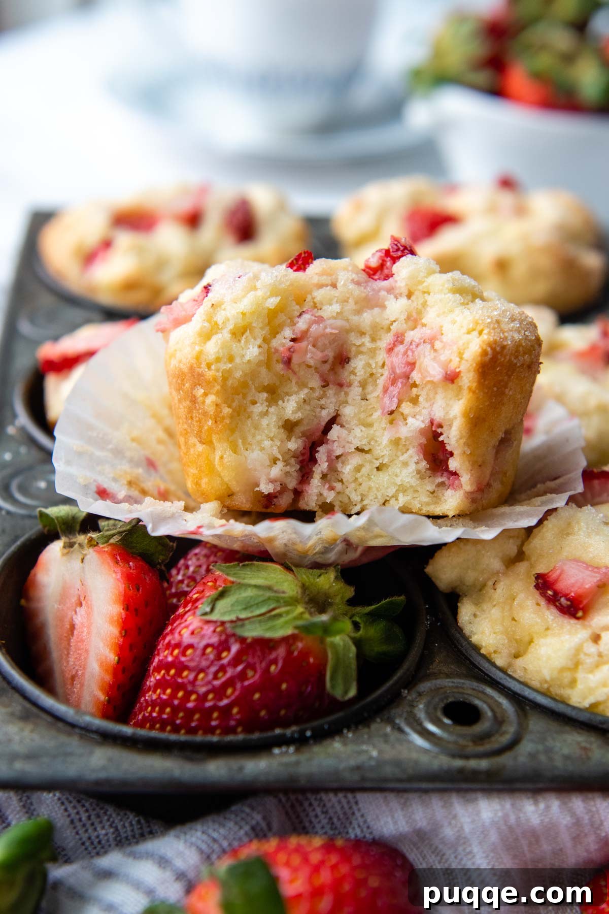 Light and Fluffy Gluten-Free Strawberry Muffins 5 A delicious gluten-free strawberry muffin, partially eaten, sits in a muffin pan with fresh strawberries in an adjacent cup.