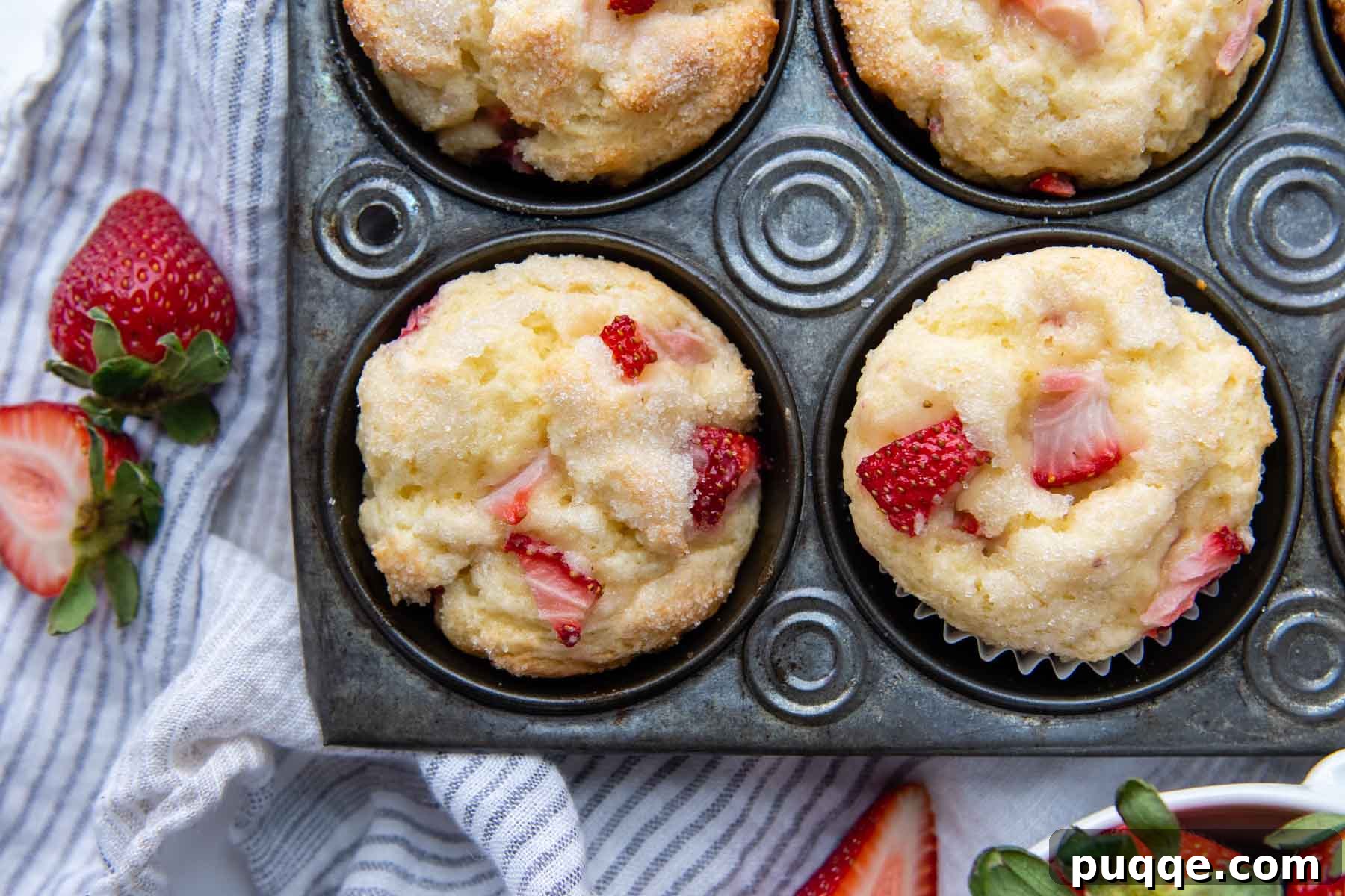 Light and Fluffy Gluten-Free Strawberry Muffins 6 An overhead shot of two fluffy gluten-free strawberry muffins in a vintage muffin pan, with fresh strawberries arranged next to it.
