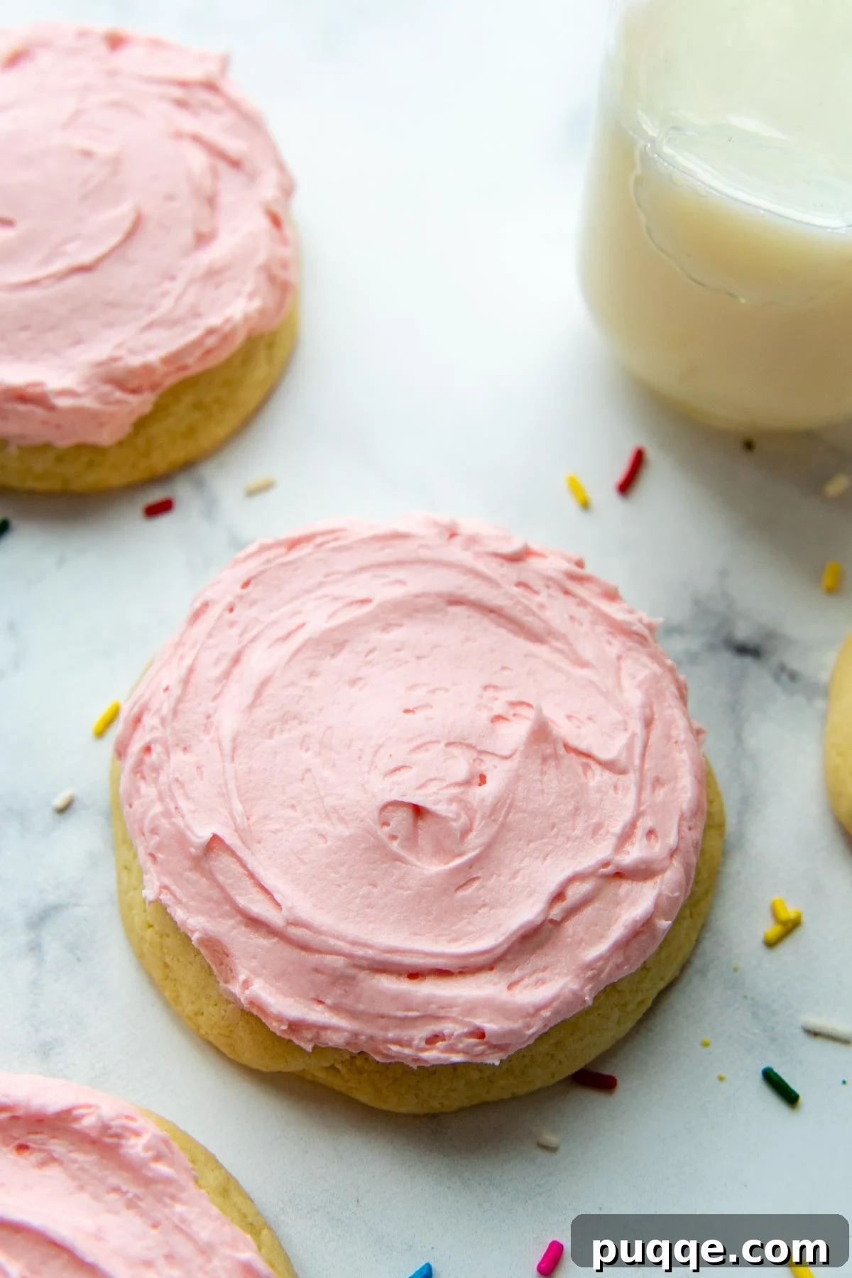 Ultimate Gluten-Free Crumbl Cookies 2 A vibrant pink sugar cookie rests on a pristine white background, adorned with playful sprinkles and accompanied by a refreshing glass of milk. This image perfectly captures the allure of our easy copycat gluten-free Crumbl cookies, promising a soft, thick sugar cookie crowned with fluffy pink frosting for an epic, irresistible dessert!