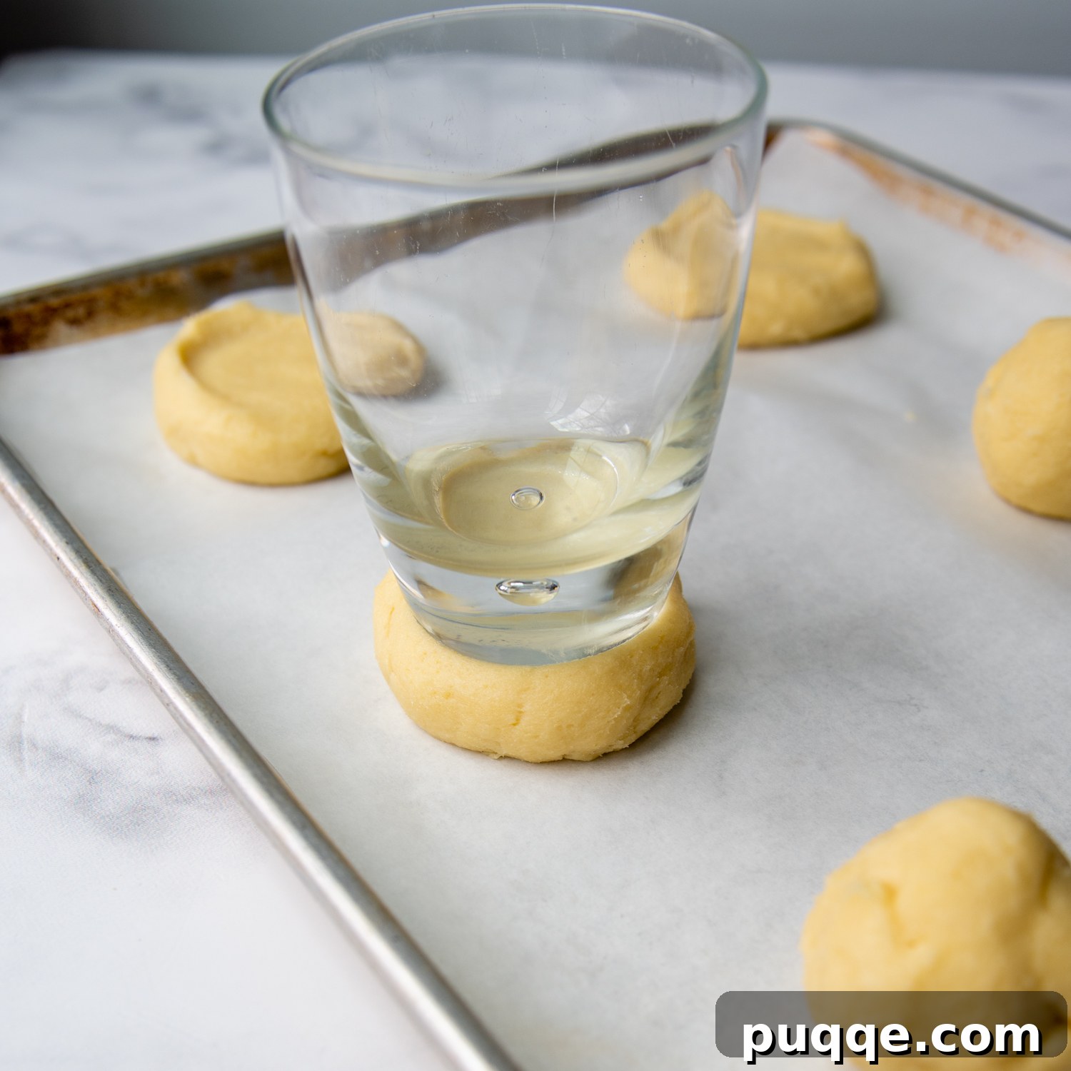 Ultimate Gluten-Free Crumbl Cookies 6 A flat-bottomed glass gently pressing down on a cookie dough ball, shaping it for baking.