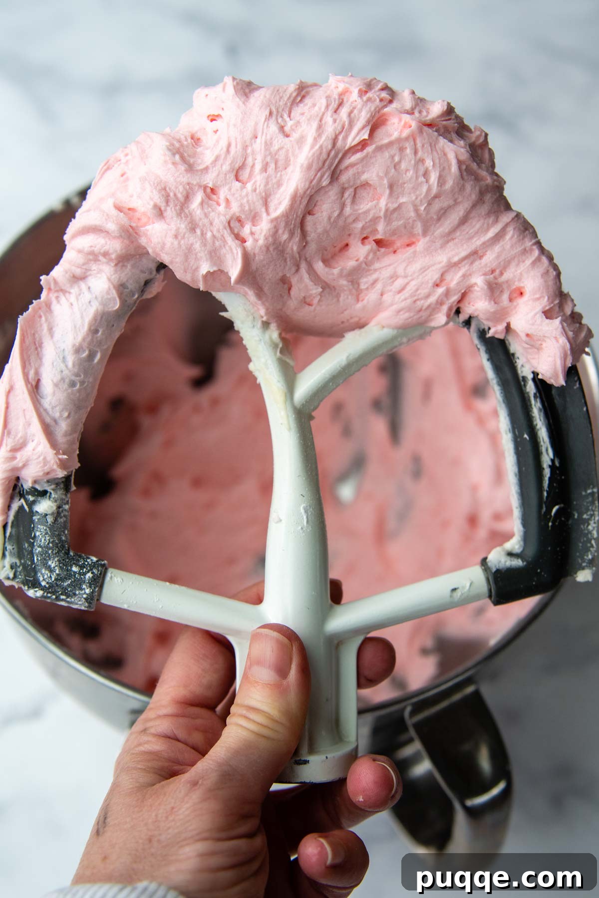 Ultimate Gluten-Free Crumbl Cookies 8 A mixer beater lifting up a generous amount of fluffy pink frosting, showcasing its light and airy texture.