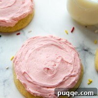 A pink sugar cookie on a white background with sprinkles around and a glass of milk, visually representing our Seriously THE BEST Gluten-Free Crumbl Cookies.