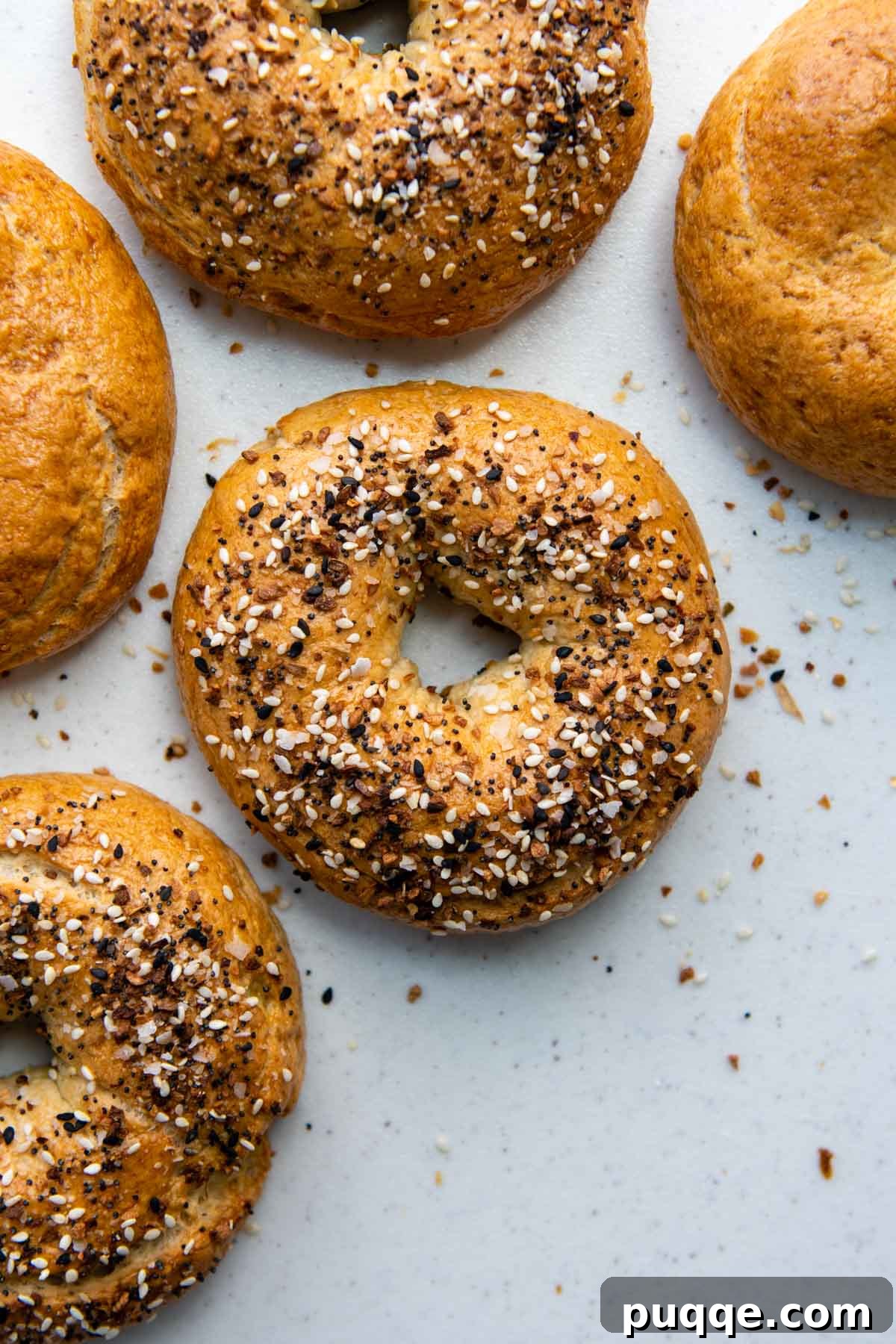 Effortless Soft & Chewy Gluten-Free Bagels 2 Overhead shot of freshly baked gluten-free bagels on a white background, showcasing their golden crust and perfect shape.