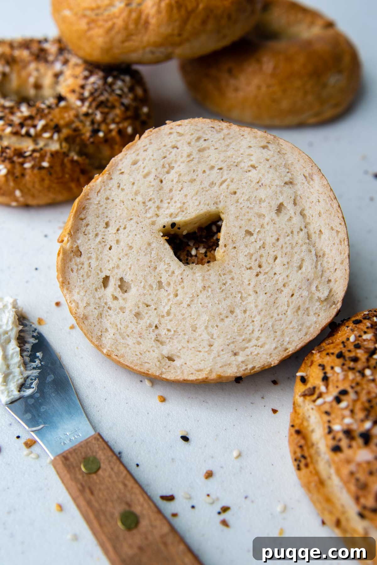 Effortless Soft & Chewy Gluten-Free Bagels 6 A perfectly sliced gluten-free bagel with other whole bagels arranged around it, showcasing the soft, doughy interior.