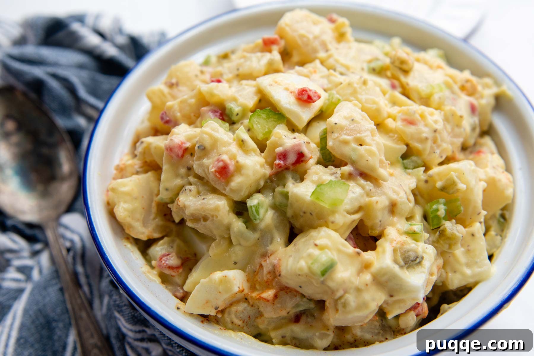 Wholesome Gluten-Free Amish Potato Salad 6 a horizontal view of a bowl of potato salad with a blue linen and serving spoon next to it.