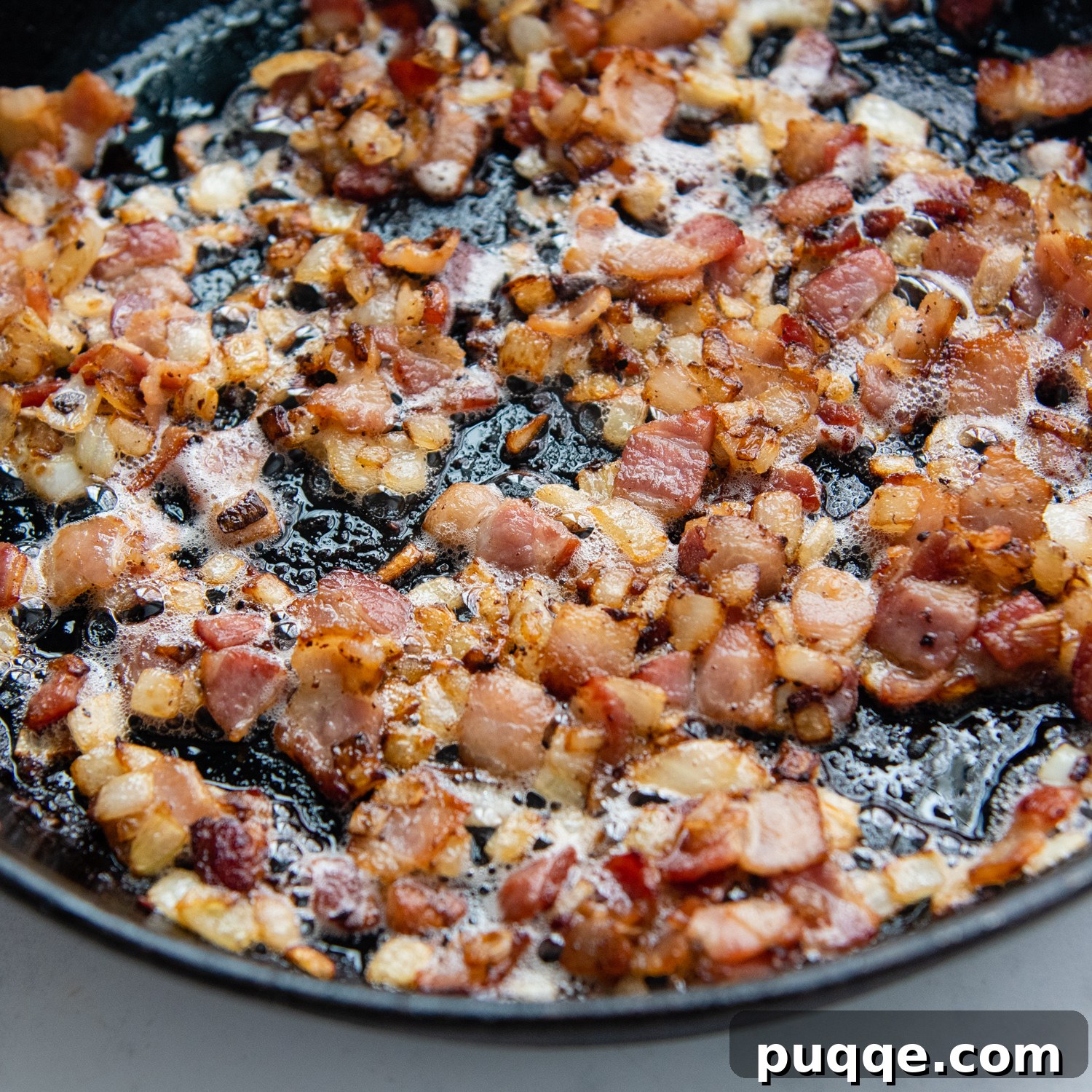 Ultimate Gluten Free Baked Beans 4 Close-up view of bacon and onions sizzling and caramelizing in a cast iron skillet.