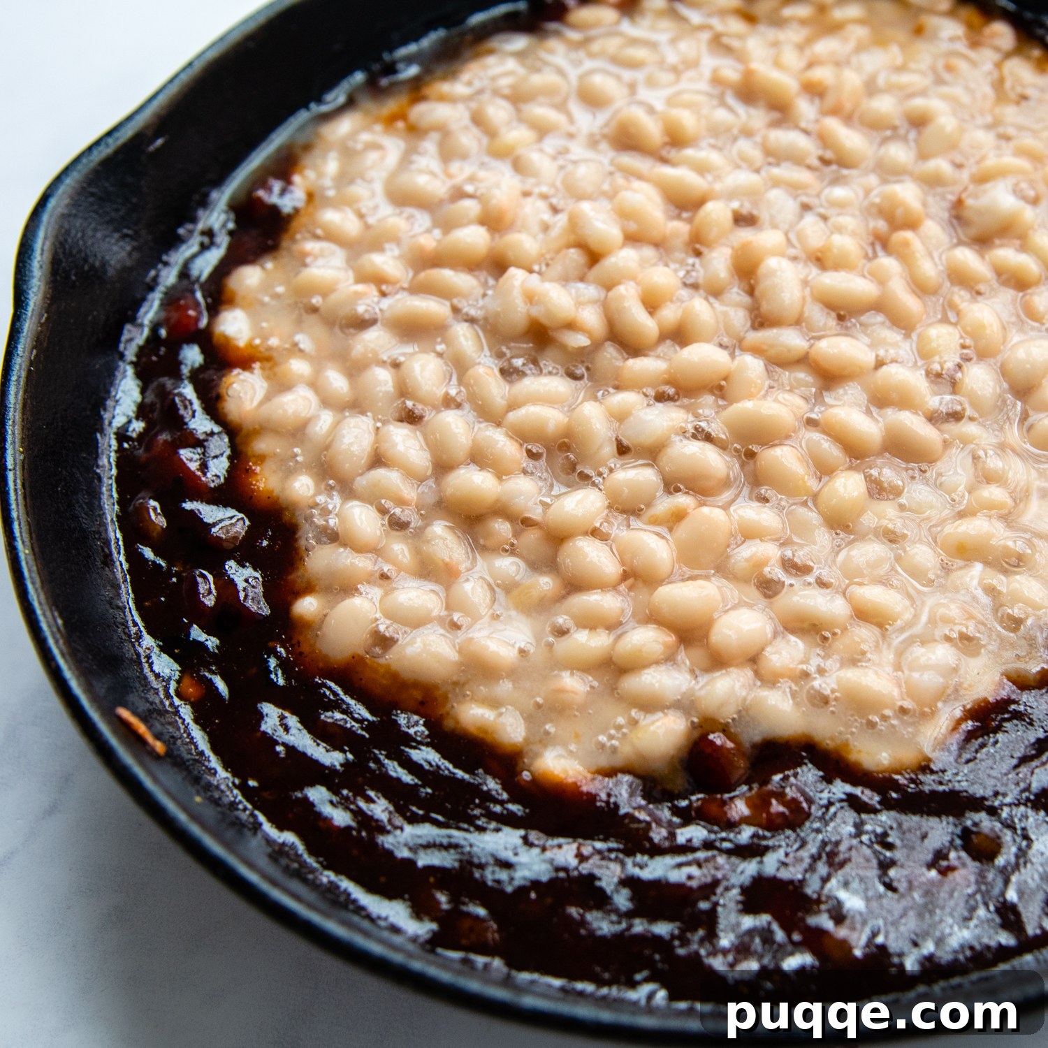 Ultimate Gluten Free Baked Beans 5 Canned beans being carefully added to the rich, simmering sauce in a skillet, ready for baking.