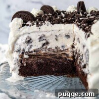 A whole gluten-free Oreo ice cream cake on a cake stand with a slice removed, showcasing its delicious layers.