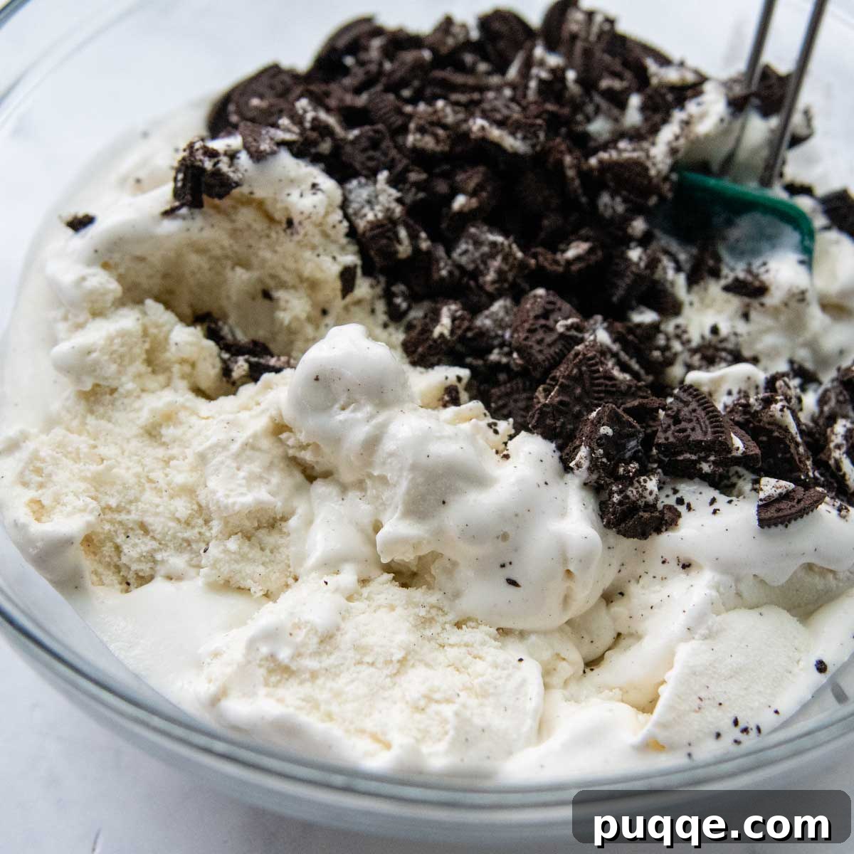 Gluten-free cookie crumbs being mixed into softened vanilla ice cream in a large bowl.