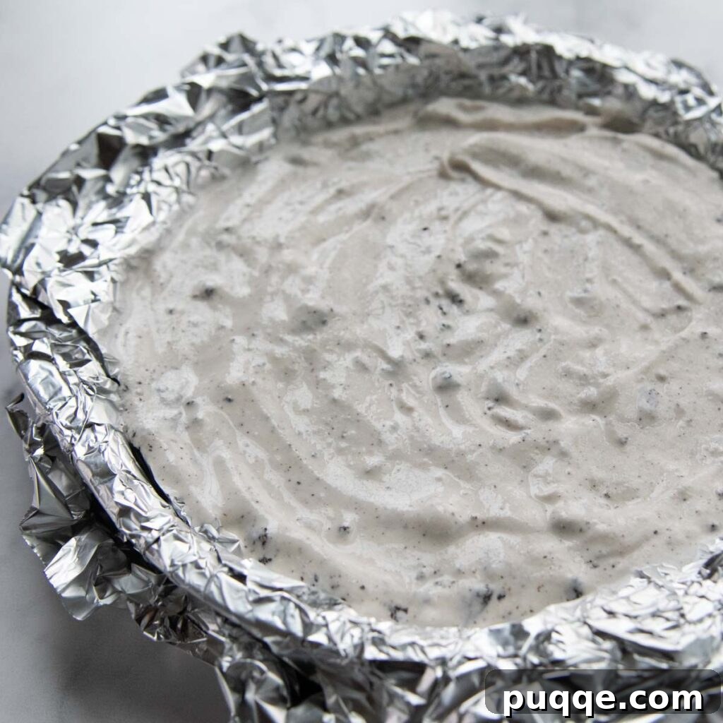 Softened ice cream mixed with cookie crumbs spread evenly in a foil-lined cake pan, ready for freezing.