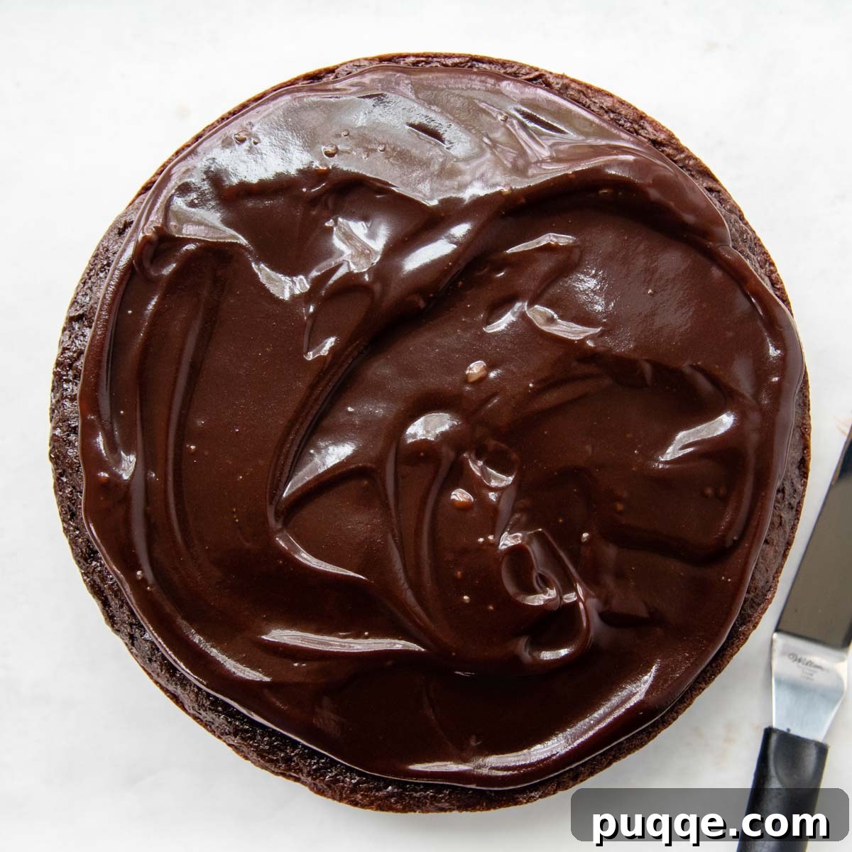 A smooth layer of hot fudge spread over the top of the cooled gluten-free chocolate cake.