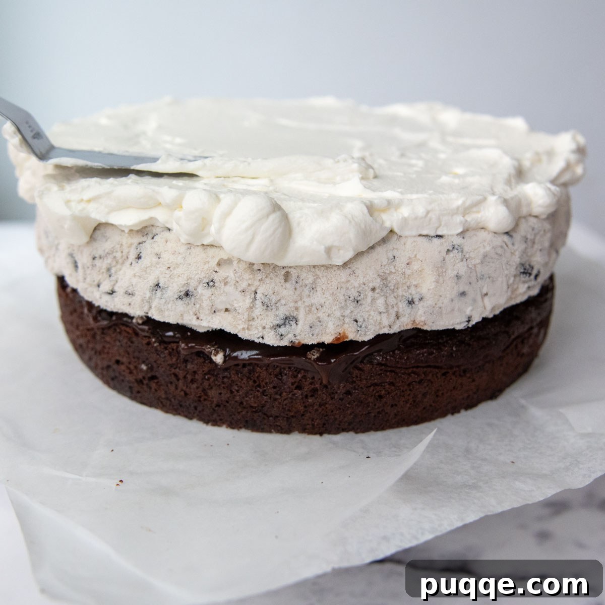 A layer of fluffy whipped cream being spread smoothly over the frozen ice cream layer on the cake.