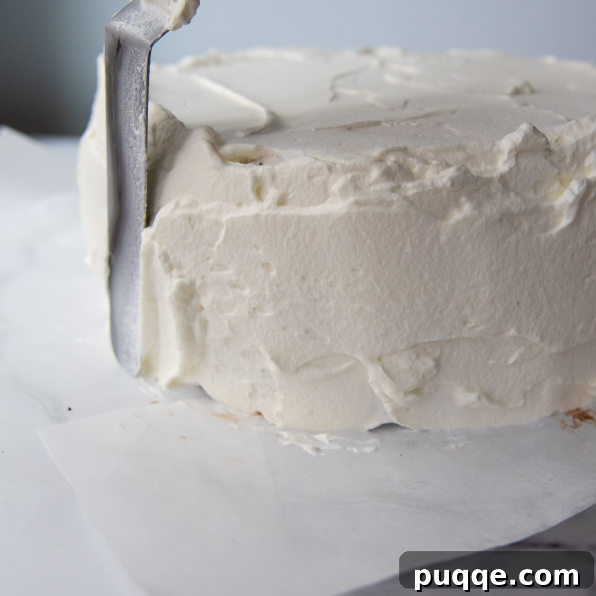 Whipped cream frosting being spread evenly on the sides of the layered ice cream cake.