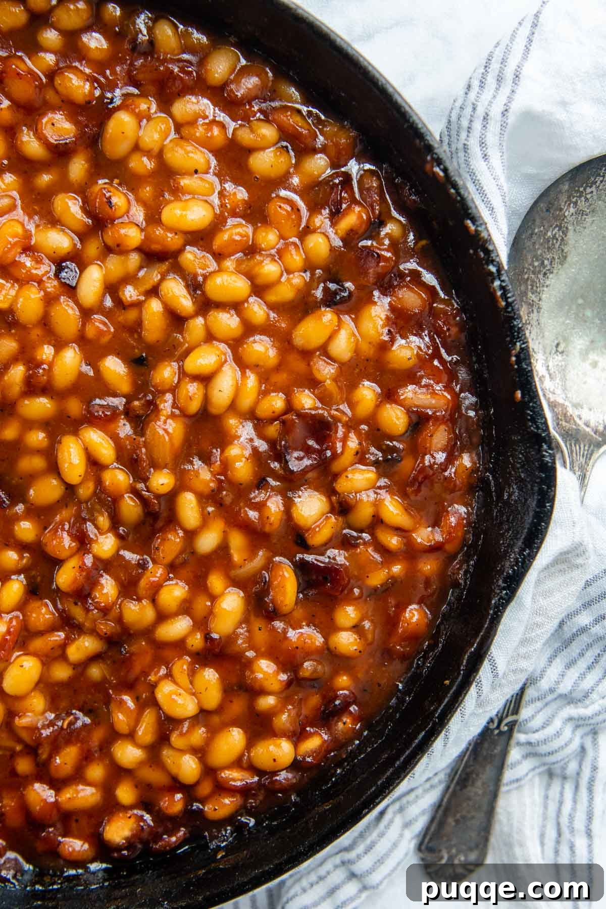 Perfect Pairings for Baked Beans 3 An inviting overhead shot of perfectly cooked baked beans simmering in a rustic cast iron skillet, with a serving spoon resting beside it, highlighting their rich texture and deep color.