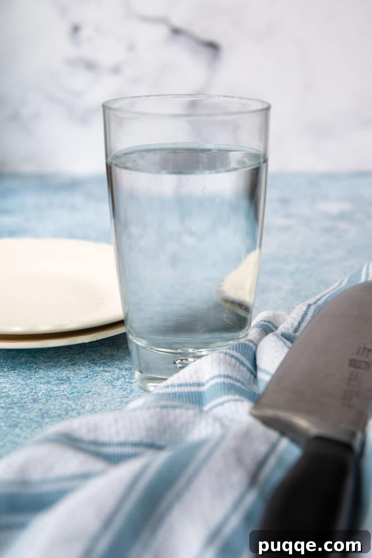 A large knife resting next to a glass of steaming hot water, prepared to be warmed for slicing a frozen cake.
