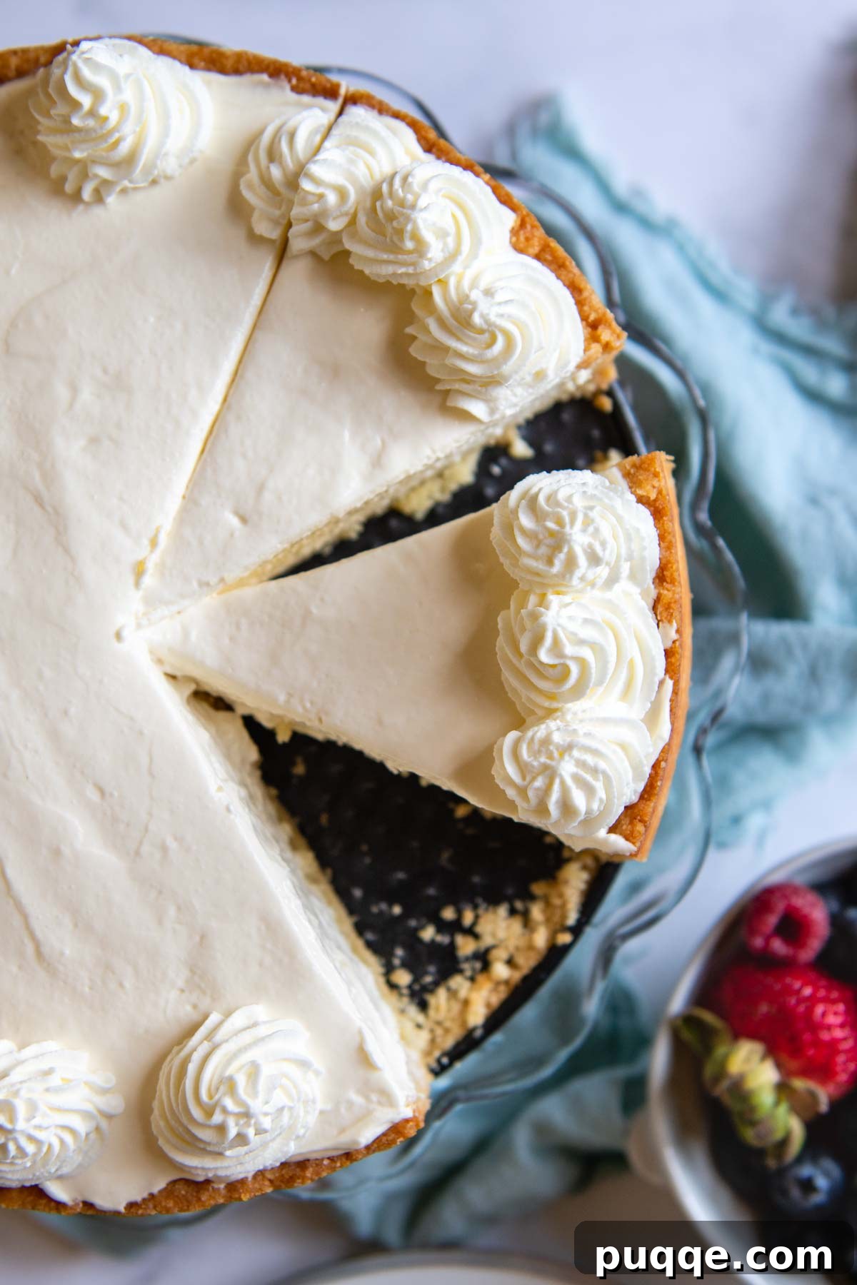 Quick Dreamy Gluten Free No Bake Cheesecake 7 An overhead shot of a perfectly sliced gluten-free cheesecake, adorned with fresh berries and served alongside a small bowl of mixed berries.