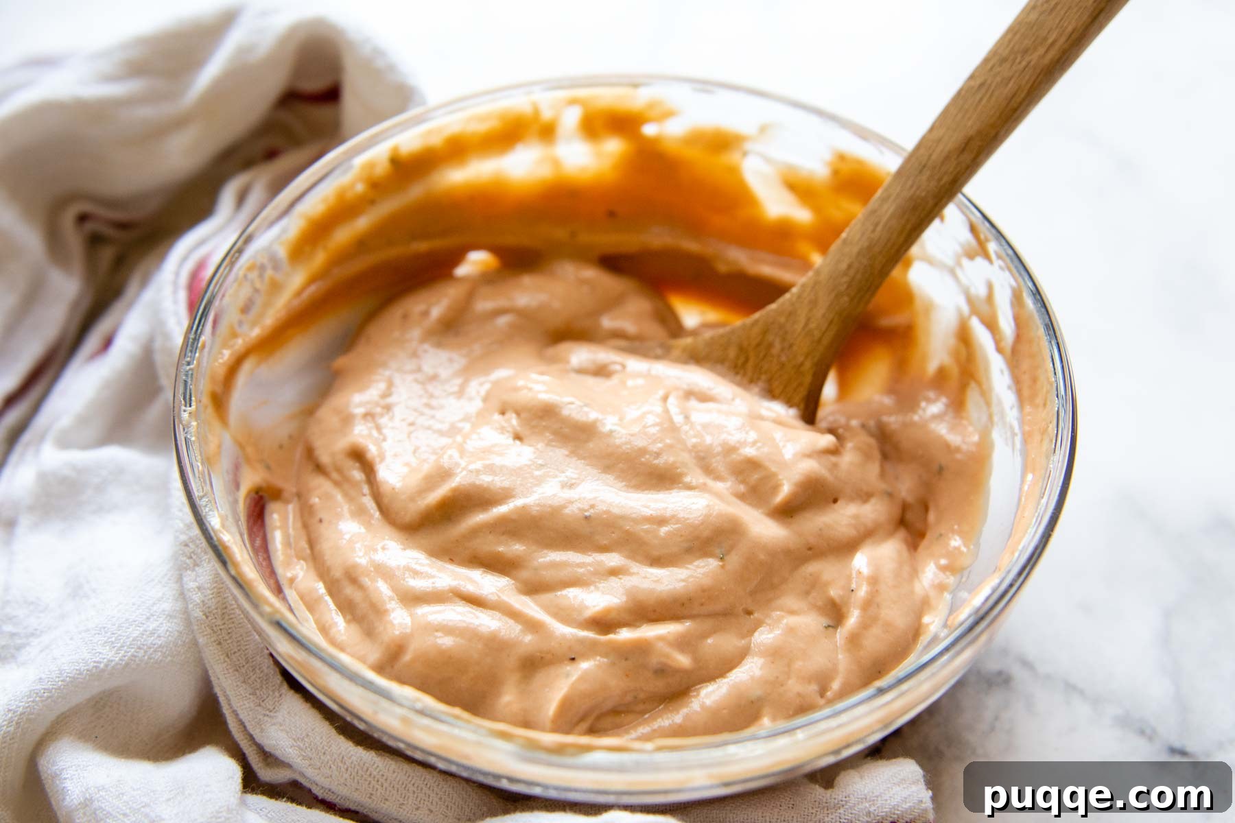 Fast BBQ Ranch Two Ways 5 A glass bowl filled with rich, creamy BBQ Ranch sauce, placed on a rustic wooden surface with a kitchen towel nearby.