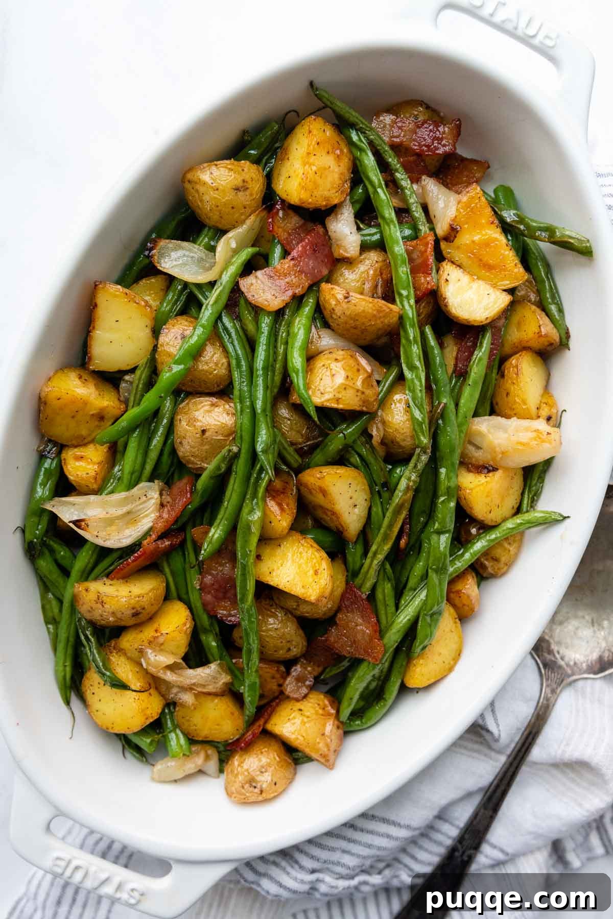 A vibrant serving dish filled with perfectly roasted green beans, crispy potatoes, caramelized onions, and savory bacon pieces, ready to be enjoyed.