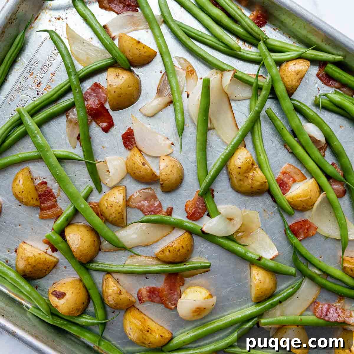 Step-by-step image showing fresh green beans added to the partially roasted potatoes, bacon, and onions on a baking sheet.