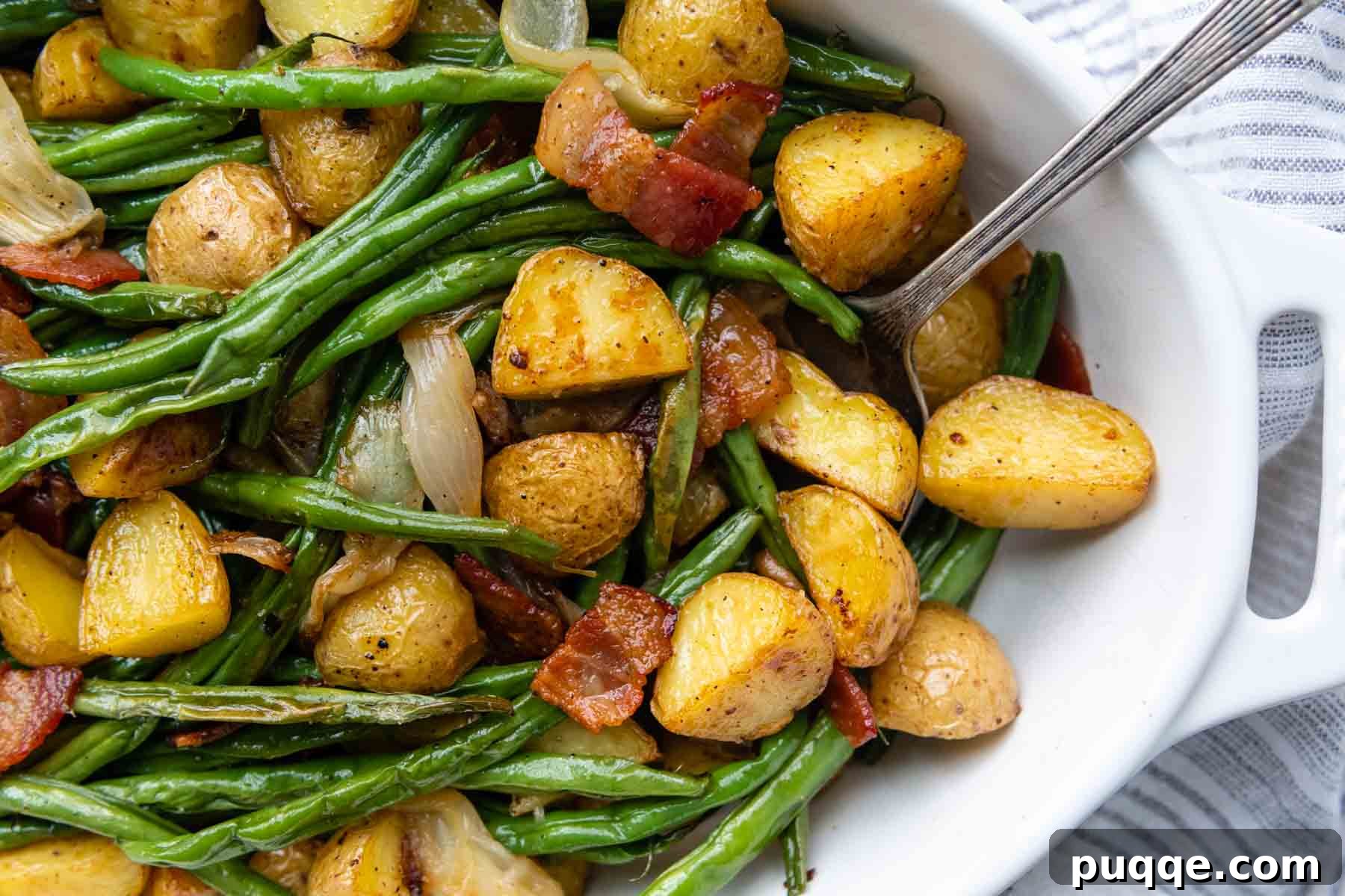 Overhead shot of a white serving dish filled with golden-brown roasted green beans and potatoes with crispy bacon, garnished for serving.