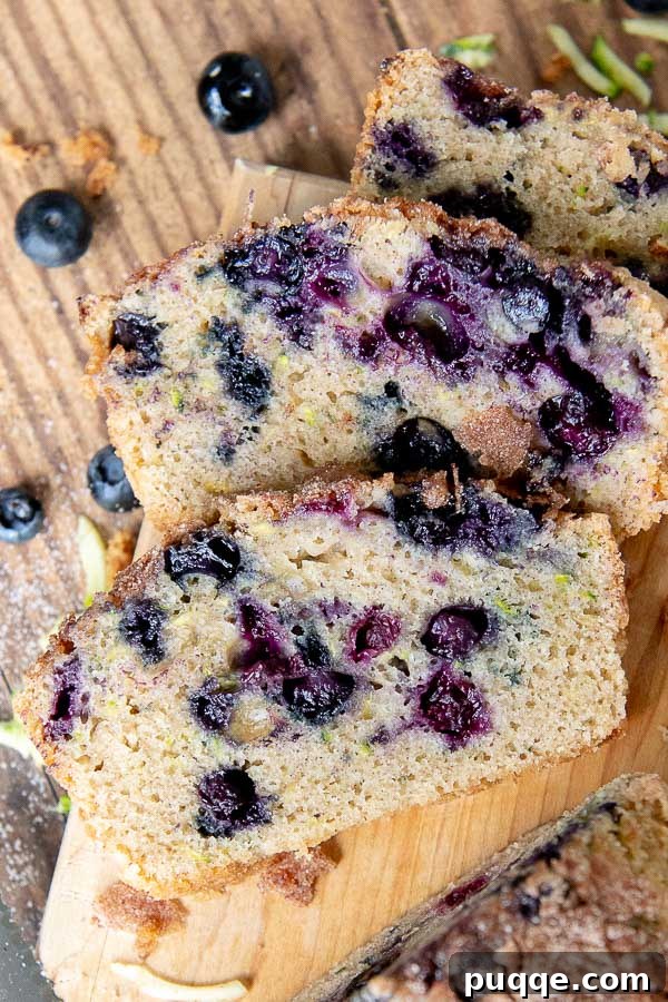 Perfectly Moist Blueberry Zucchini Bread 2 Overhead shot of moist blueberry zucchini bread slices on a wooden cutting board, featuring a crisp cinnamon sugar topping and visible blueberries and zucchini specks.