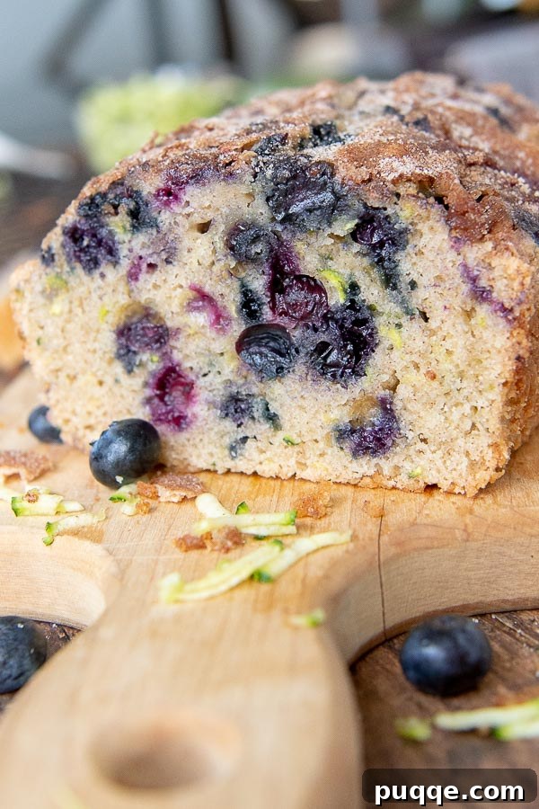 Perfectly Moist Blueberry Zucchini Bread 7 A perfectly baked loaf of moist blueberry zucchini bread on a cutting board, with one inviting slice already cut and ready to eat.