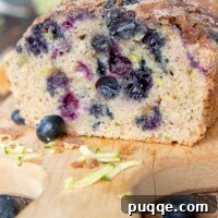 A loaf of moist blueberry zucchini bread on a cutting board with a slice taken out, highlighting its delicious texture.