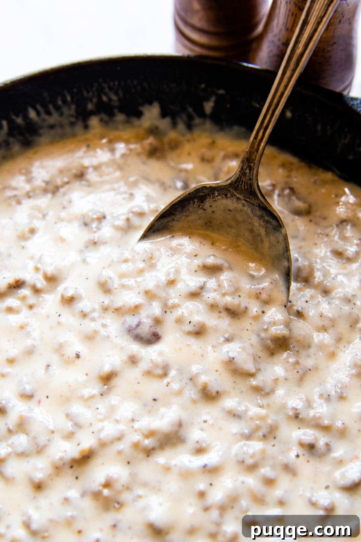 Effortless 10-Minute Gluten-Free Sausage Gravy 6 Close-up of an antique spoon dipping into a skillet of bubbling, creamy gluten-free sausage gravy.