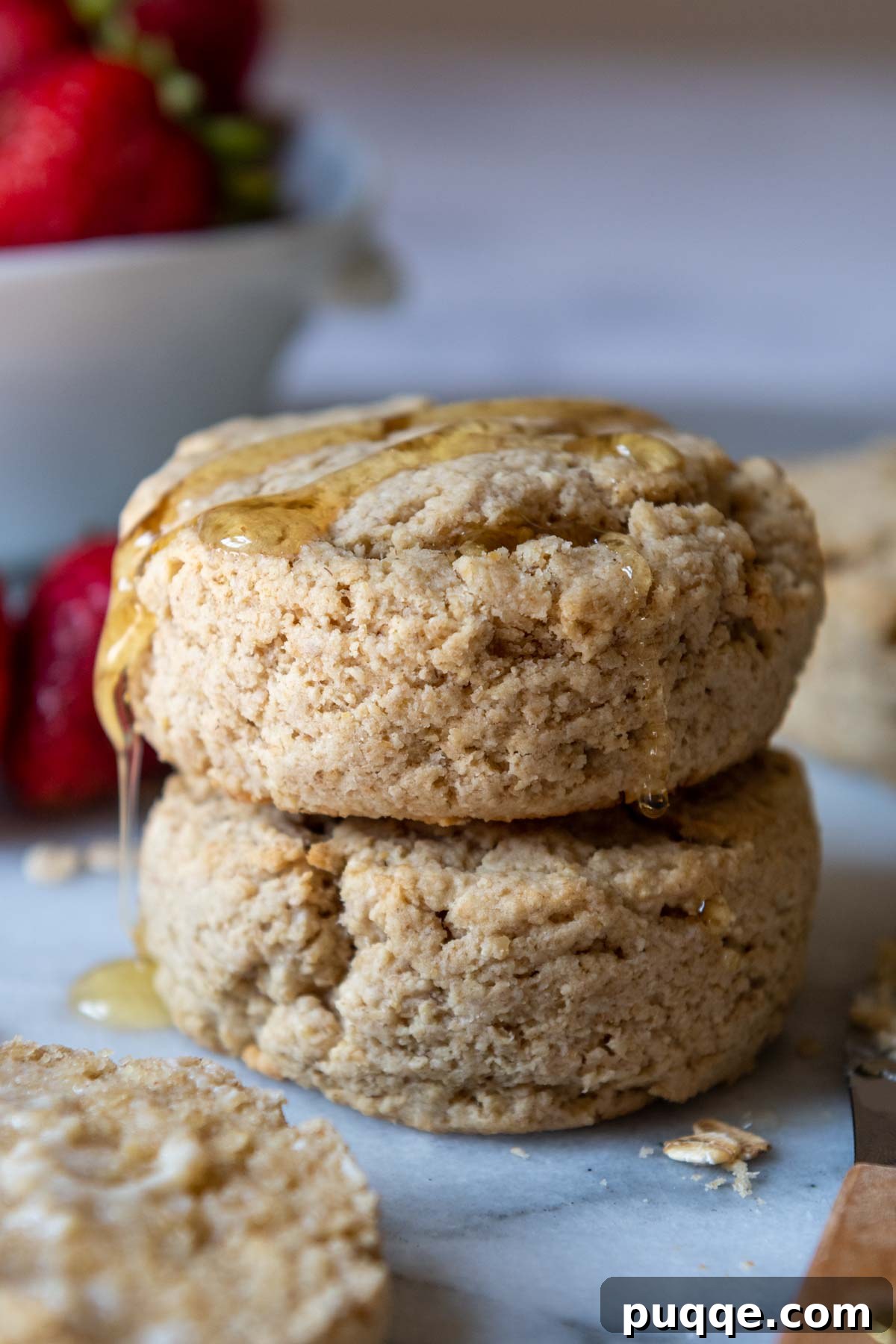 A stack of two fluffy oat flour biscuits with golden honey dripping over the top.
