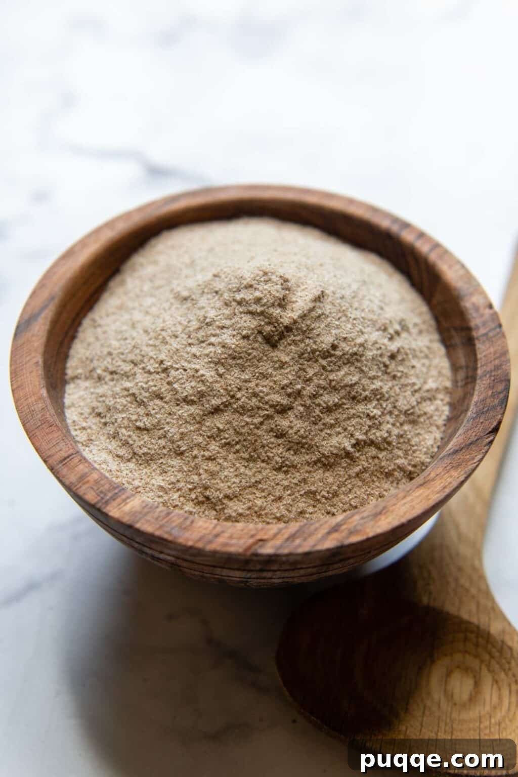 A wooden bowl filled with psyllium husk powder, with a measuring spoon resting beside it, ready for gluten-free baking, illustrating its common use.