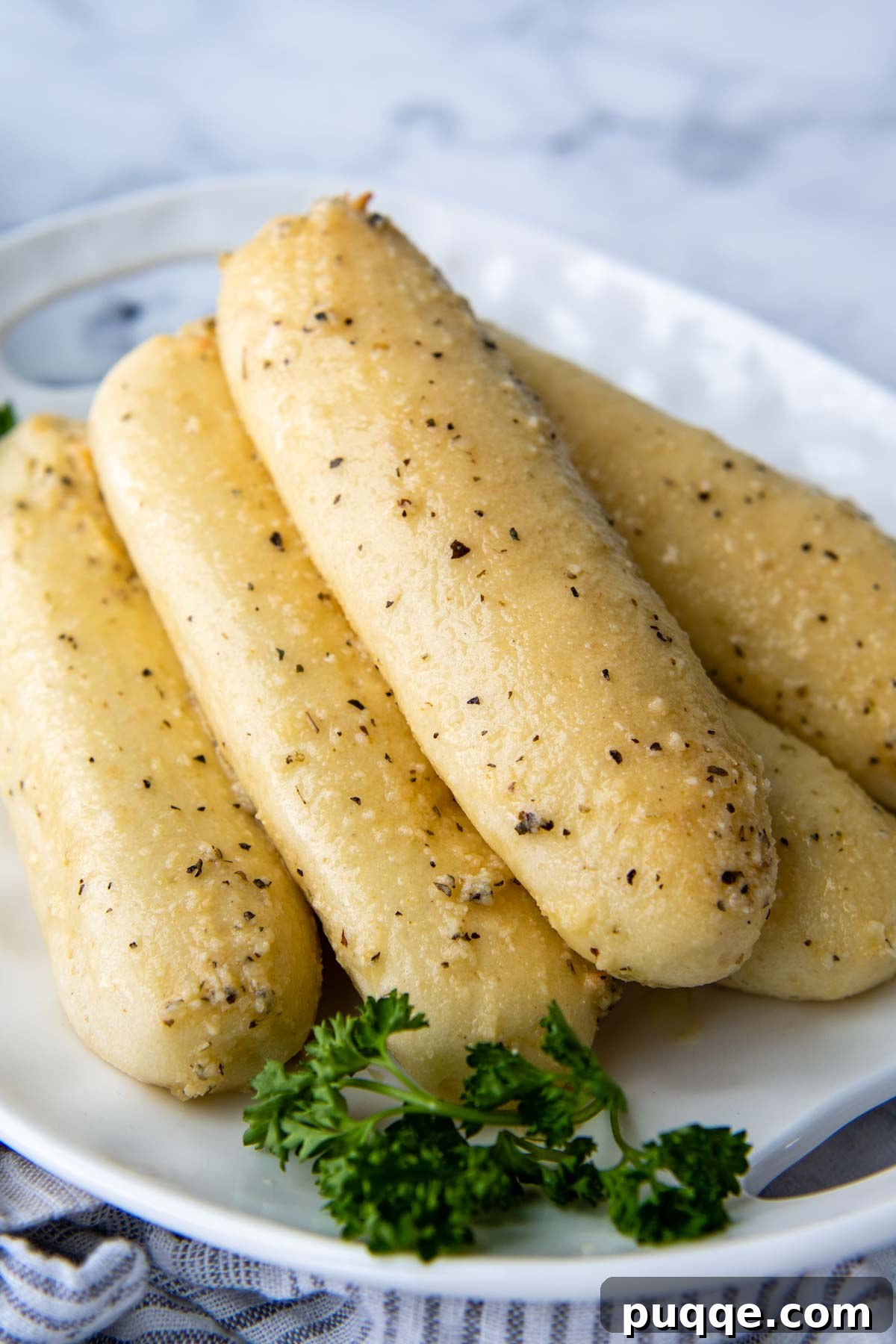 Warm gluten-free breadsticks stacked on a white plate with fresh parsley, inviting a delicious bite.