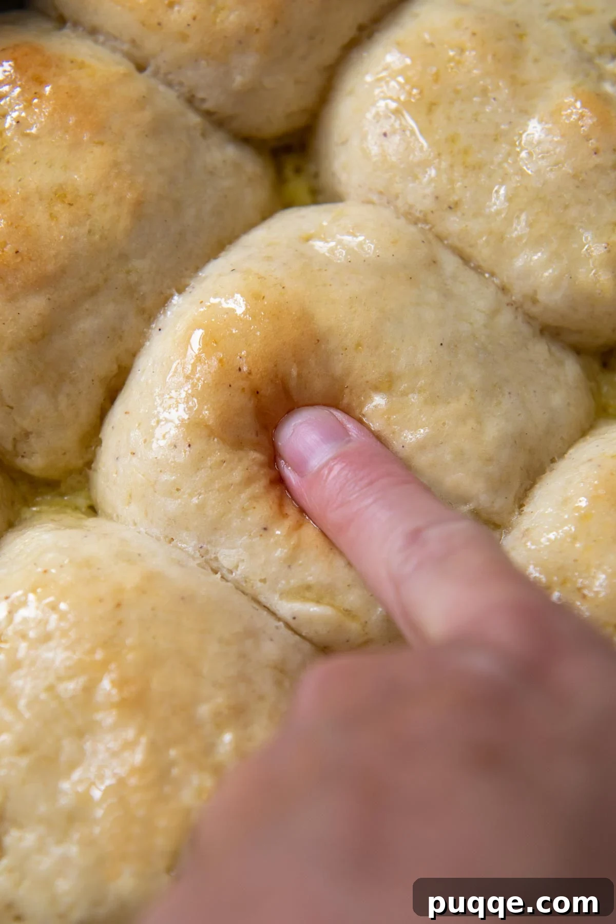 A finger gently pressing into the top of a fluffy gluten-free roll, demonstrating its perfect softness.