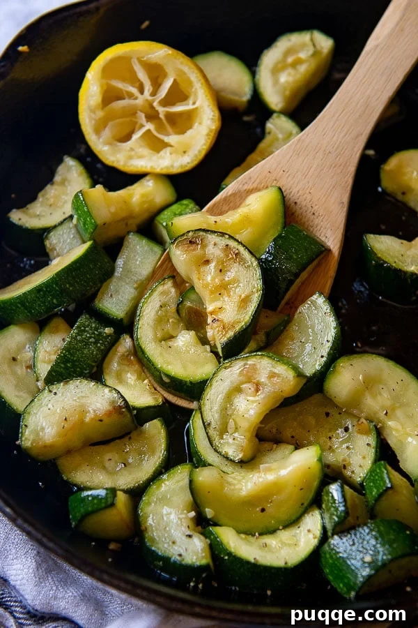 Close-up shot of cooked zucchini being lifted from a pan with a wooden spoon, garnished with fresh herbs.