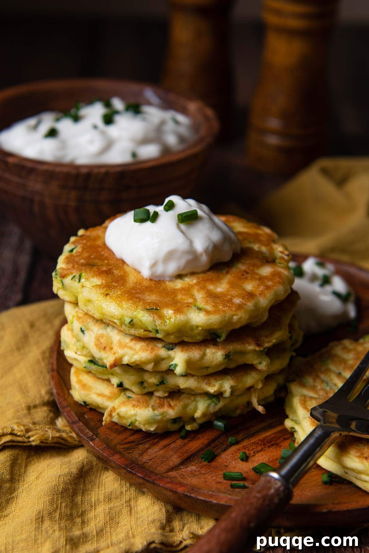 A stack of golden zucchini fritters on a rustic wooden plate, with a decorative gold napkin underneath.